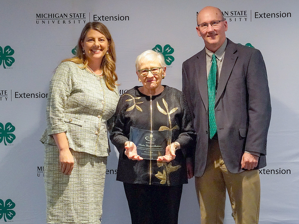 Three individuals at a backdrop. The center person holds an award.